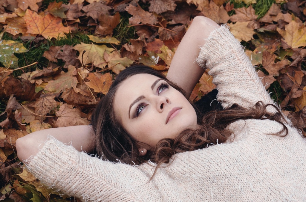 Reflective and graceful brunette Albanian woman lying peacefully in autumn leaves