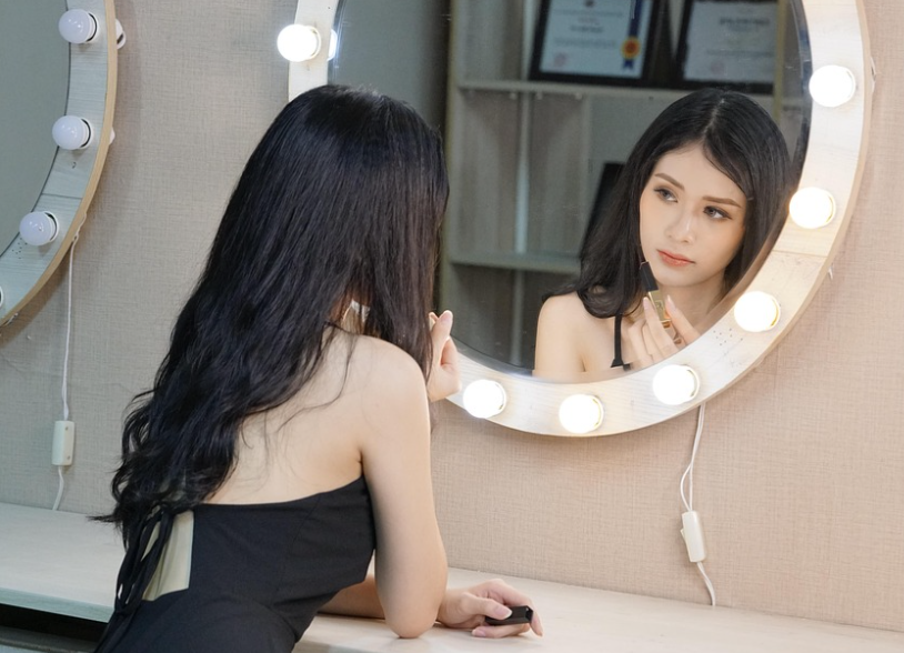 Beautiful Asian woman applying makeup looking in vanity mirror