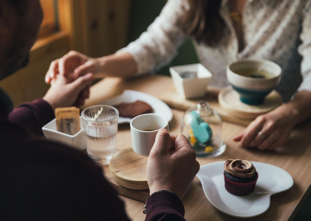 Genuine intimate coffee date between international couple holding hands across wooden table