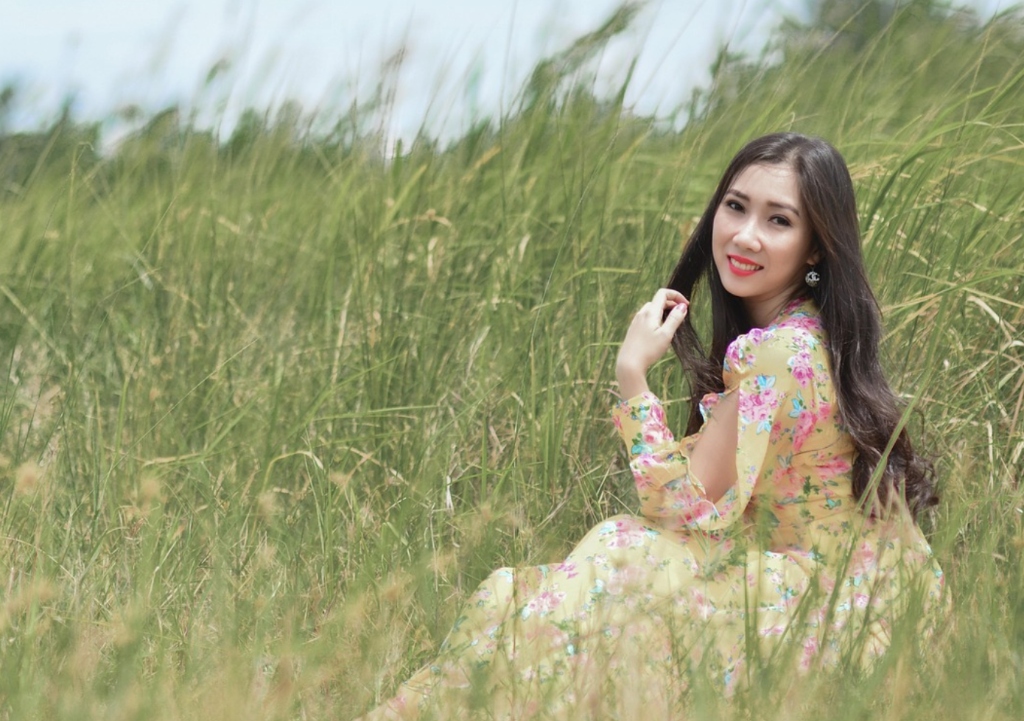 Gentle and feminine Chinese woman in floral yellow dress amidst peaceful green landscape