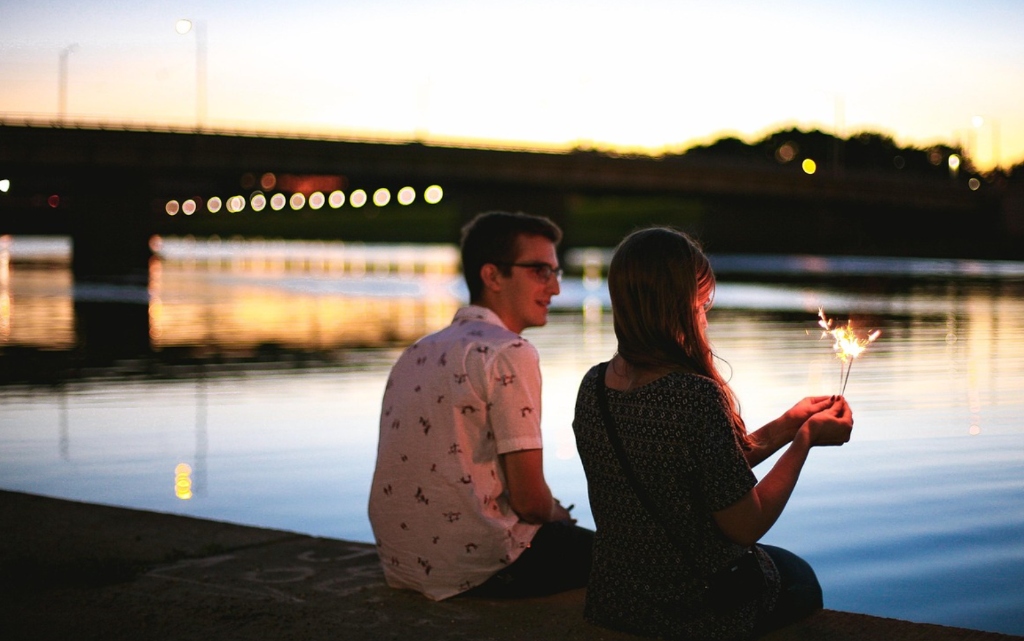 Genuine international couple sharing romantic sunset moment by river with sparkler - authentic chemistry