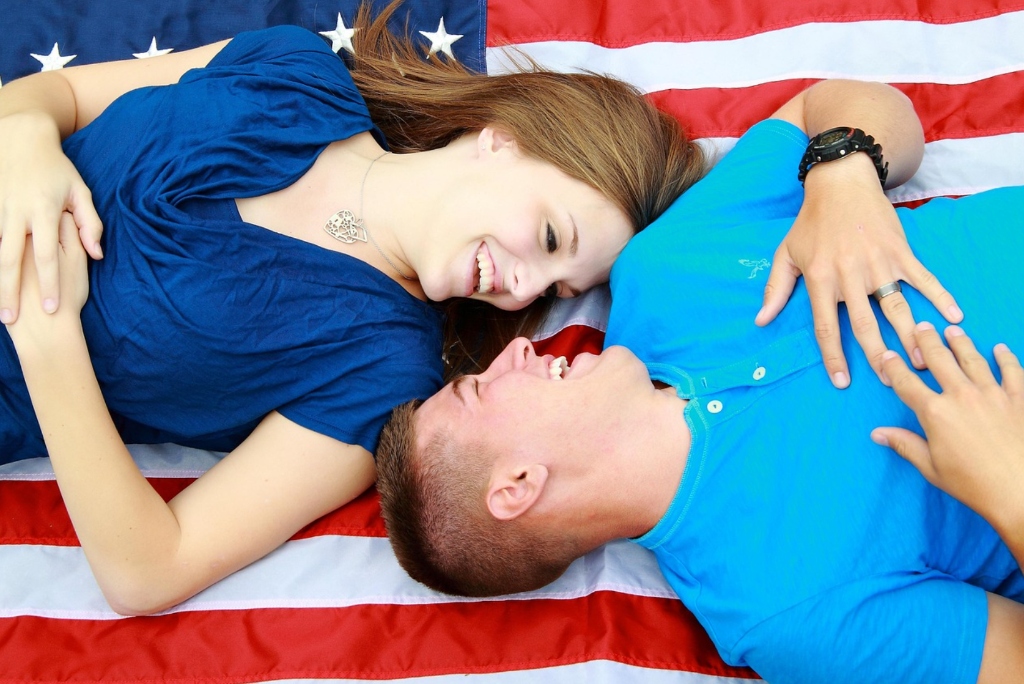 Happy international marriage couple holding US flag celebrating legal K-1 visa and lawful citizenship