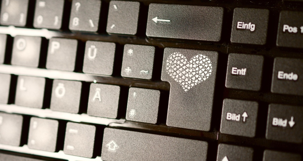 Computer keyboard with illuminated heart button representing online romance scams and digital catfishing