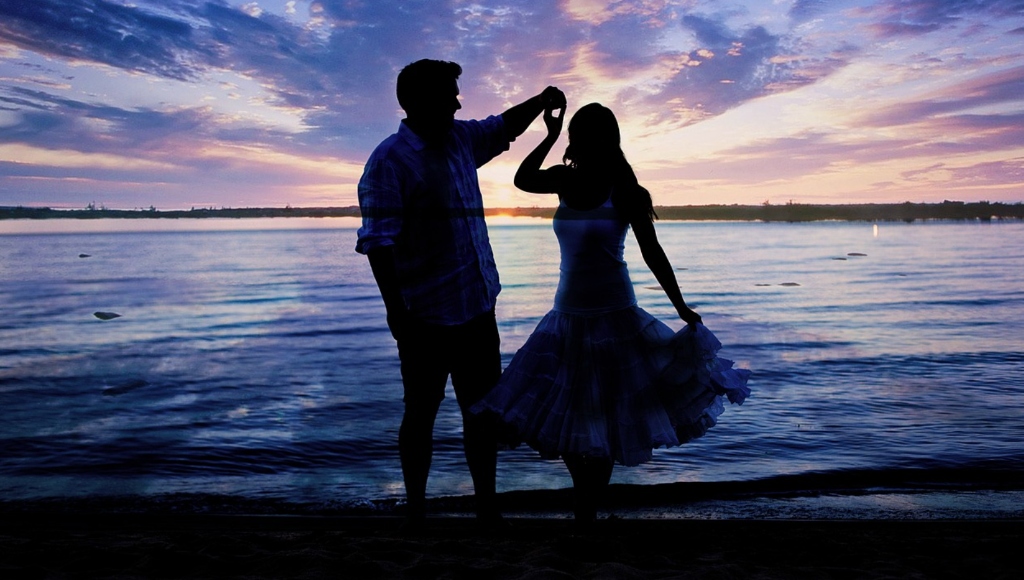 Silhouette of international couple dancing on beach at colorful twilight sunset - authentic marriage