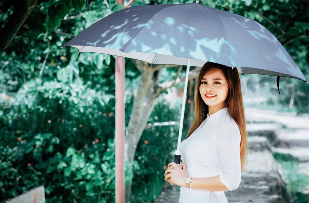 Gentle Thai woman in white dress holding umbrella in peaceful nature - traditional grace
