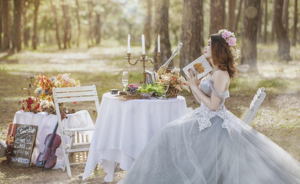 Fairytale Slavic bride in romantic ballgown with book at beautifully decorated outdoor forest banquet table