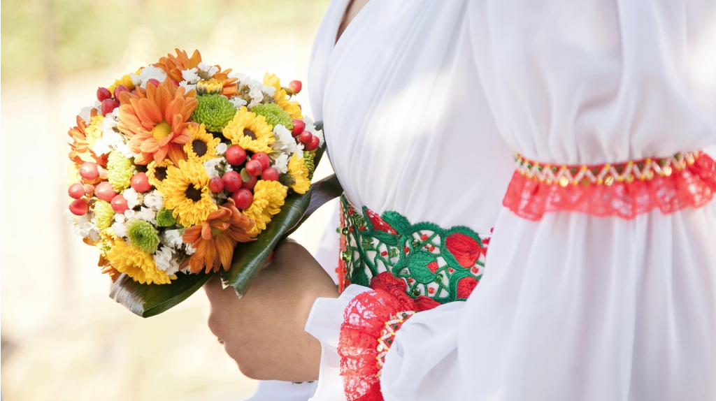 Traditional Ukrainian bride wearing elegant embroidered white vyshyvanka dress holding sunflower bouquet