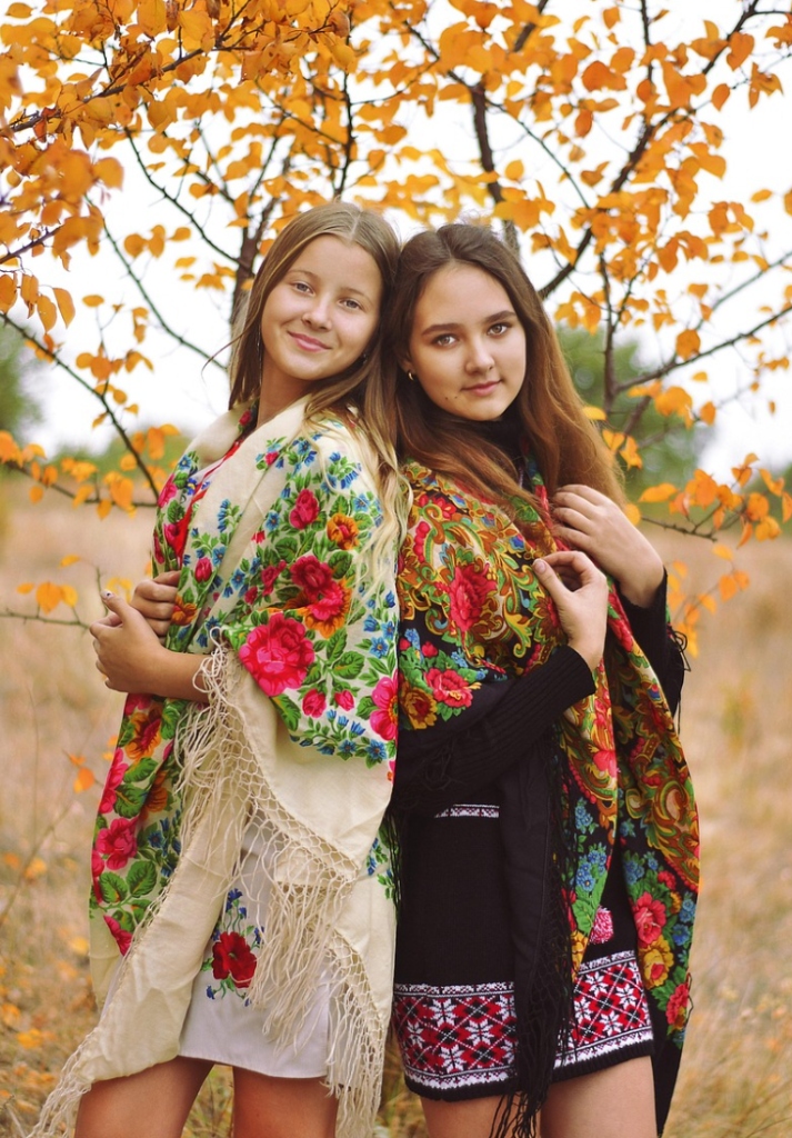 Two beautiful Ukrainian young women wearing traditional floral Slavic shawls back to back in autumn nature